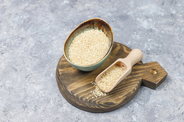 Bowl of tahini with sesame seeds on concrete background